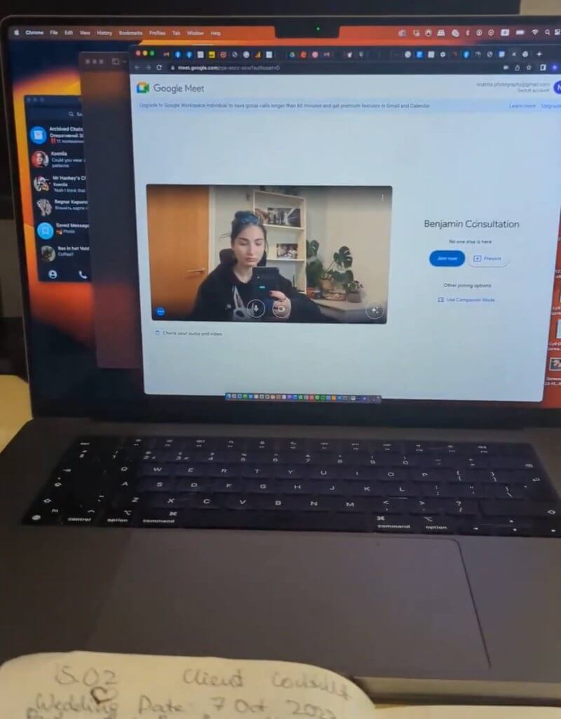 A laptop screen shows a Google Meet video call with someone indoors, sporting long dark hair in a dark top. Below the screen lies a notebook filled with handwritten notes. Perhaps they're jotting down tips to find the perfect wedding photographer!.